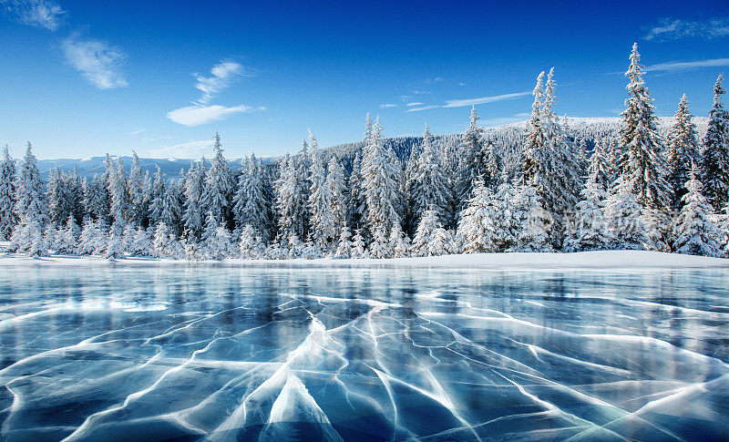 蓝色的冰和冰表面的裂缝。冬天蓝天下的冰湖。松树山。冬天。喀尔巴阡、乌克兰、欧洲。