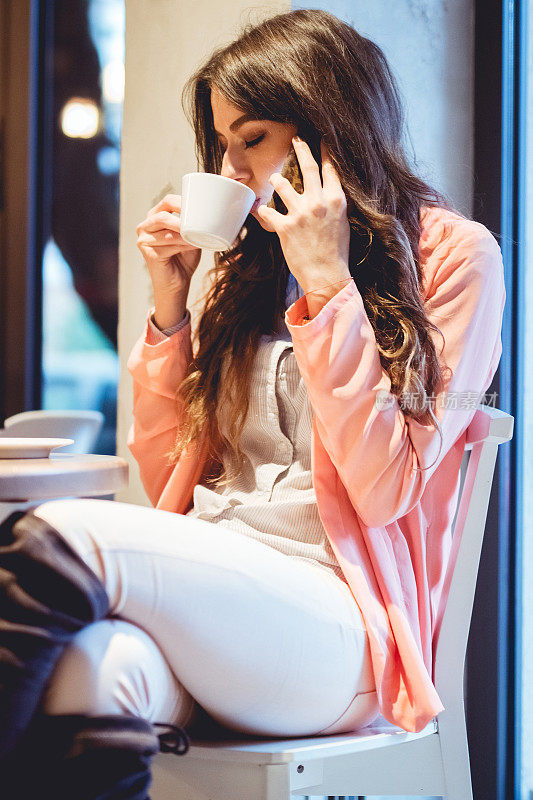 现代女孩坐在桌边喝着咖啡，用着手机。