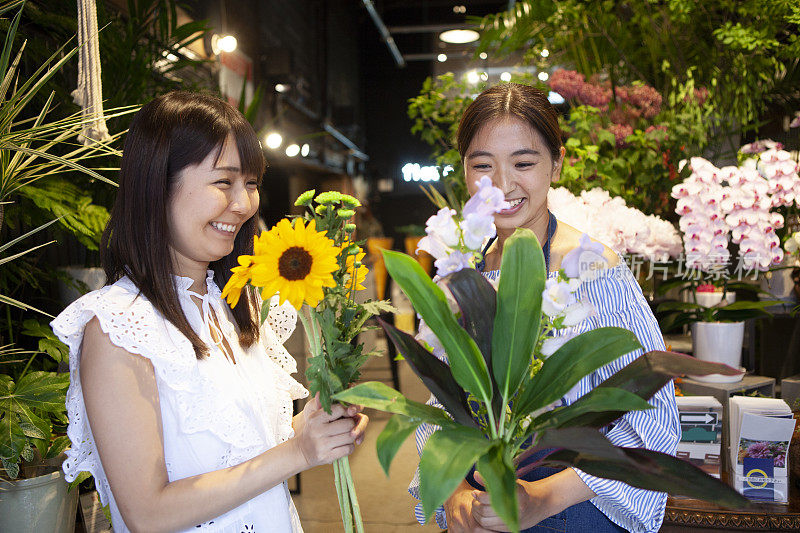 在花店里帮助一位挑选向日葵和树叶的妇女的店员。