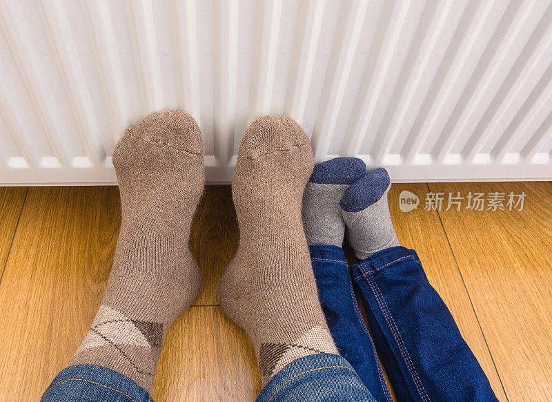 父子俩穿着冬天的羊毛袜子，在暖气片旁暖脚。家用燃气锅炉或电加热器。