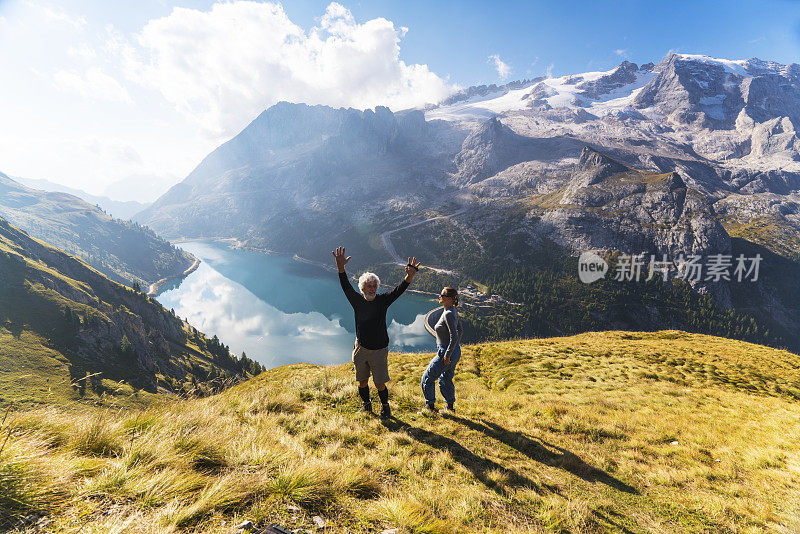 在意大利北部Dolomites的Fedaia山口到Pordoi山口的小路上休息的老年人夫妇正在欣赏美丽的Fedaia湖和马尔莫拉达山的景色。