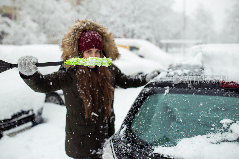 年轻女子在清理车上的积雪