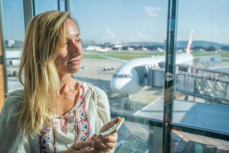 年轻女子在机场等待航班时用智能手机发短信