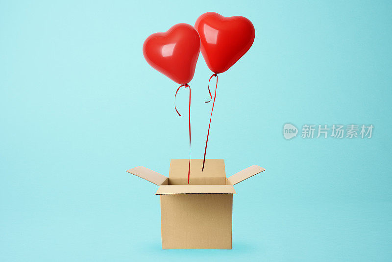两个红色的心形气球漂浮在一个纸板箱上