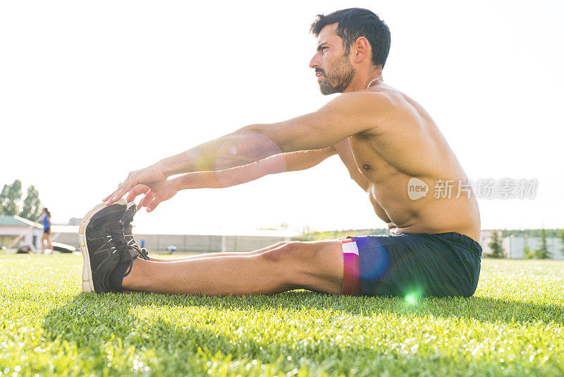 一个阳光明媚的日子，运动员在跑道上热身。一个男性运动员的肖像热身和伸展