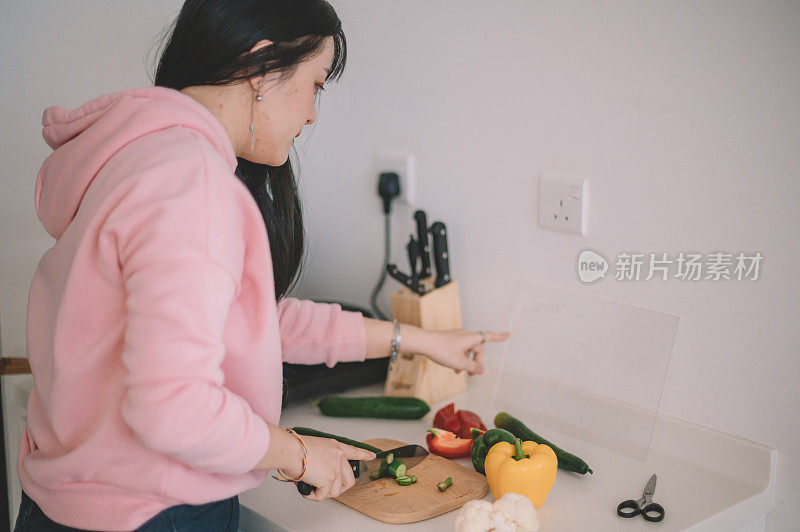 一名亚洲华裔年轻女子正在准备晚餐，并在厨房里查阅食谱的透明数字平板电脑