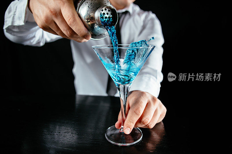 调酒师将蓝色鸡尾酒倒入马提尼酒杯