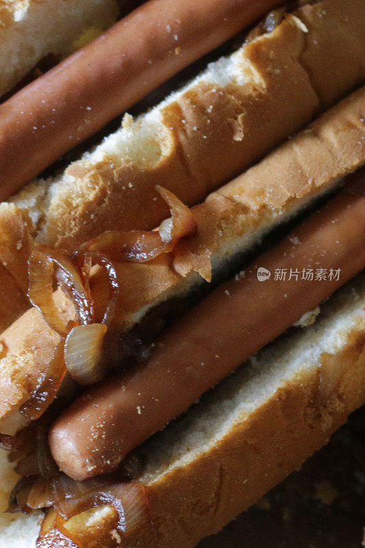 一组热狗和炸洋葱放在木砧板上，热狗面包夹着法兰克福香肠和熟洋葱