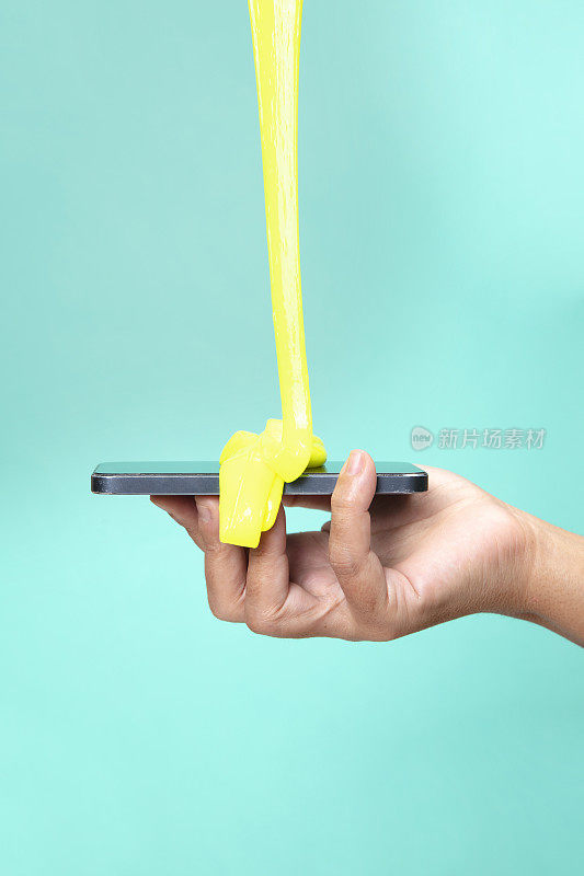 女人的手用智能手机与霓虹灯黄色黏液玩具在绿色波普艺术背景。