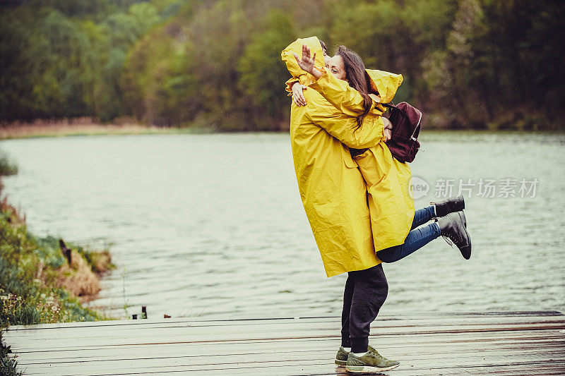 拥抱一对穿着雨衣在雨中徒步旅行的情侣