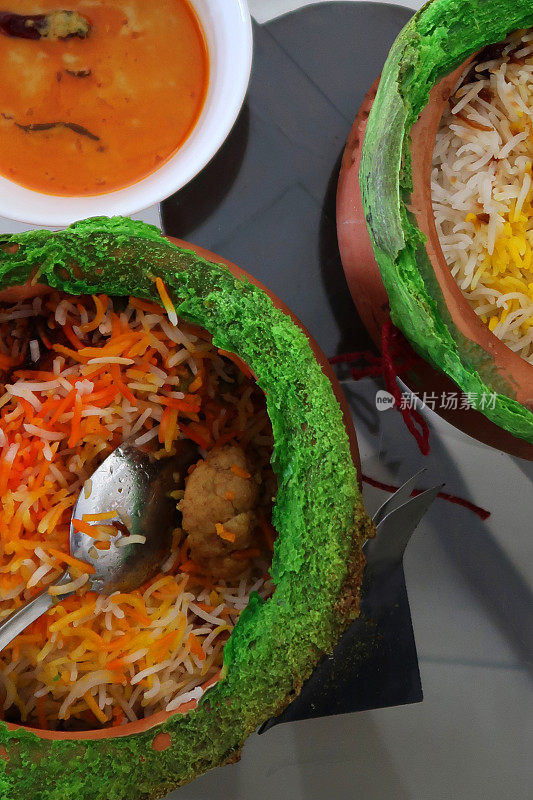 近距离图像的金属勺子在赤陶罐包含印度外卖米饭，鸡肉biryani与鸡masala肉汁酱在玻璃桌上