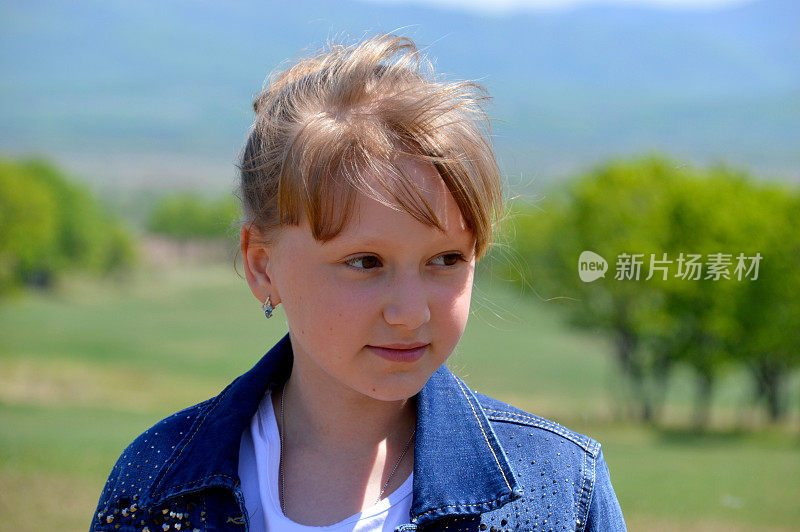 肖像10岁的俄罗斯金发女孩微笑在绿色的田野背景。可爱的脸，看着别处