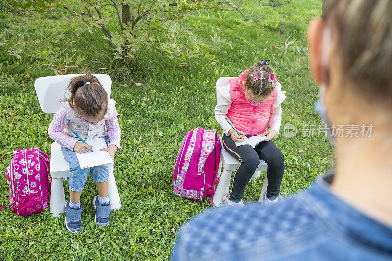 一位戴着防护面罩的老师在一个改良的户外课堂上教她的小女生写作