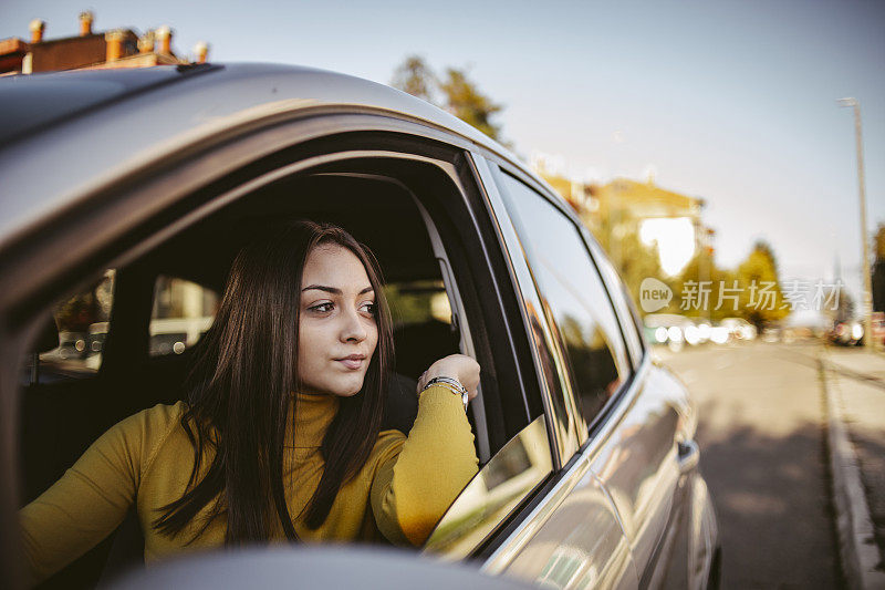 年轻的学生骄傲地坐在她的新车-快乐的司机驾驶一辆车-一个快乐的细心的司机女人驾驶一辆车在道路上的肖像