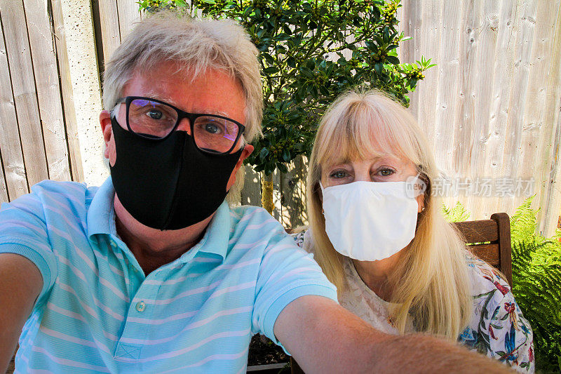 一对戴着防护面罩的老年夫妇在花园里一起自拍