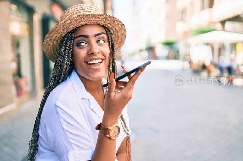 年轻的非洲裔美国妇女与辫子愉快地使用智能手机在一个阳光明媚的夏天户外
