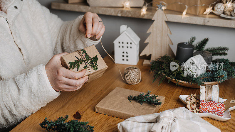 圣诞节零浪费环保再利用包装礼品过程。零浪费可重复使用的工艺纸可持续的礼物用工艺纸与绿叶在家里的桌子上