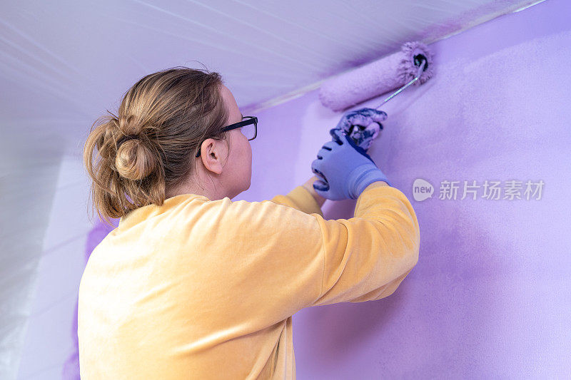 女设计师用滚筒在墙上涂上颜色，很有活力地翻新舒适的家