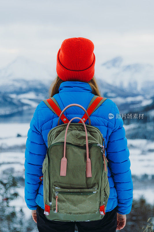 背着双肩包的女人从上面看着戏剧性的冬季山景，沉思着雪