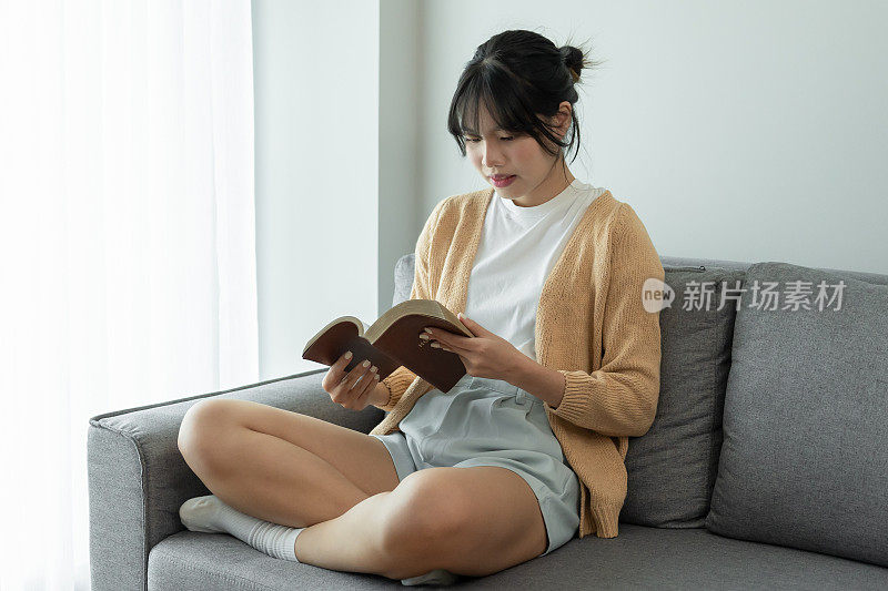 快乐的女人在看书，舒舒服服地放松。Â女性手中拿着bookÂ在家学习概念读物