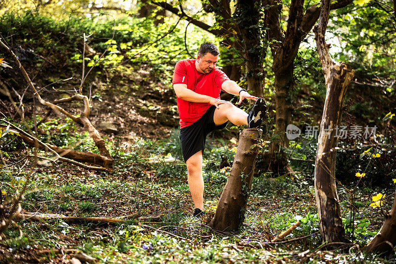 中年男性慢跑者在森林里伸展腿筋