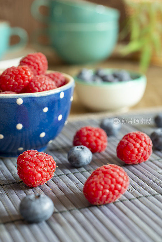 蓝碗里的Rapsberries放在桌子上，装饰有蓝莓和黑莓