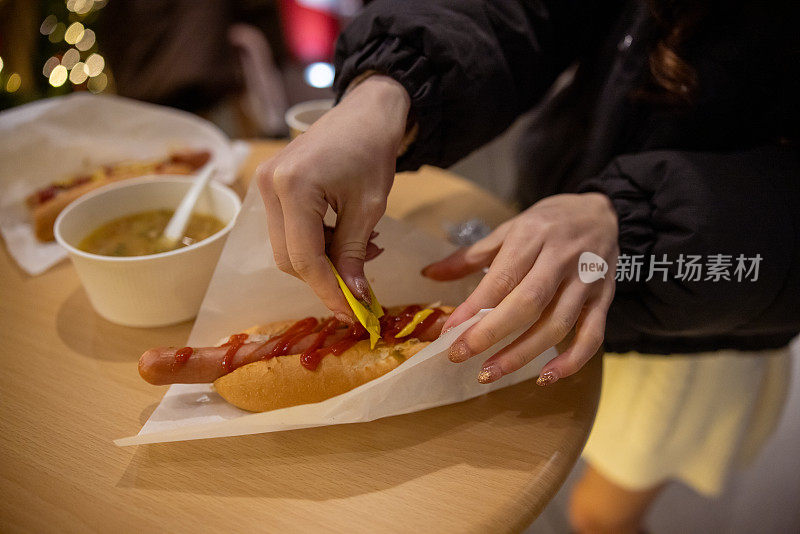 年轻女子在基督市场把番茄酱和芥末酱涂在热狗上