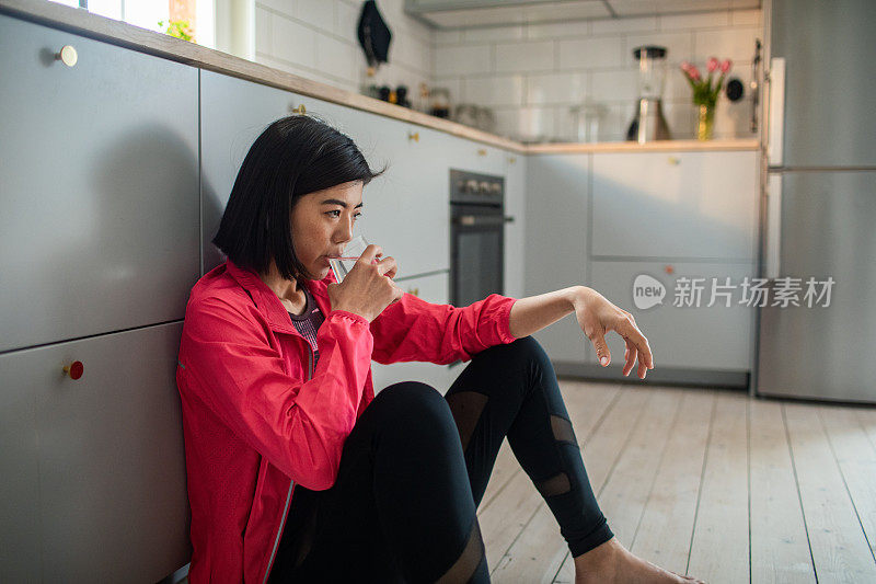 年轻的成年女性在锻炼后在厨房喝着一杯水