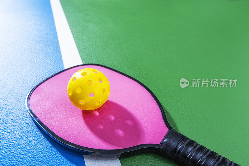 一个粉红色的匹克球球拍和一个黄色的球放在球场上