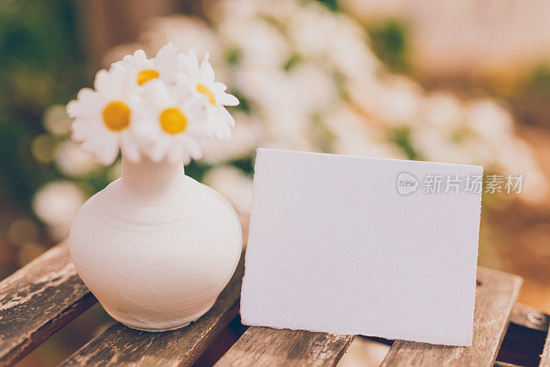 可爱的花瓶，白色的雏菊和一张空的明亮的纸作为复活节的模型，春夏短信放在一个小乡村桌子上