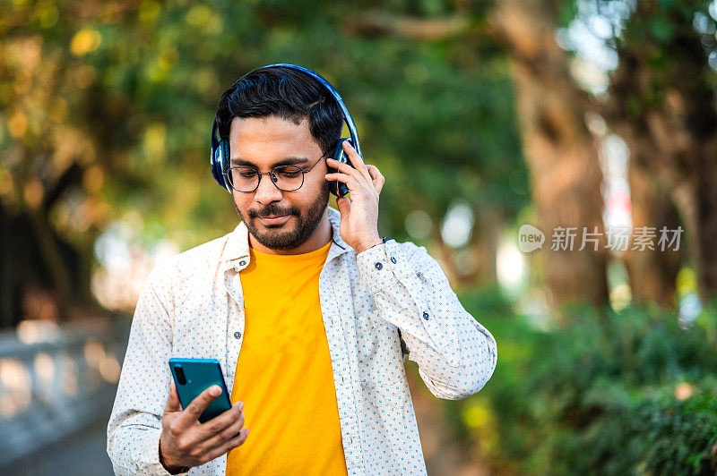 年轻的亚洲男子在市中心，使用手机和耳机