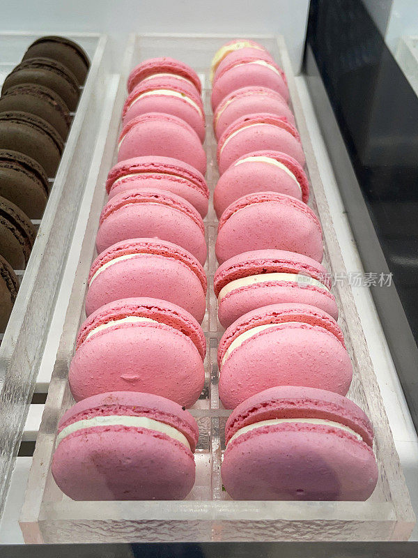 面包店托盘展示的特写图像，成排的粉红色和棕色马卡龙填充了调味黄油奶油，一口大小的草莓和巧克力味蛋白霜三明治饼干，高视图，重点在前景
