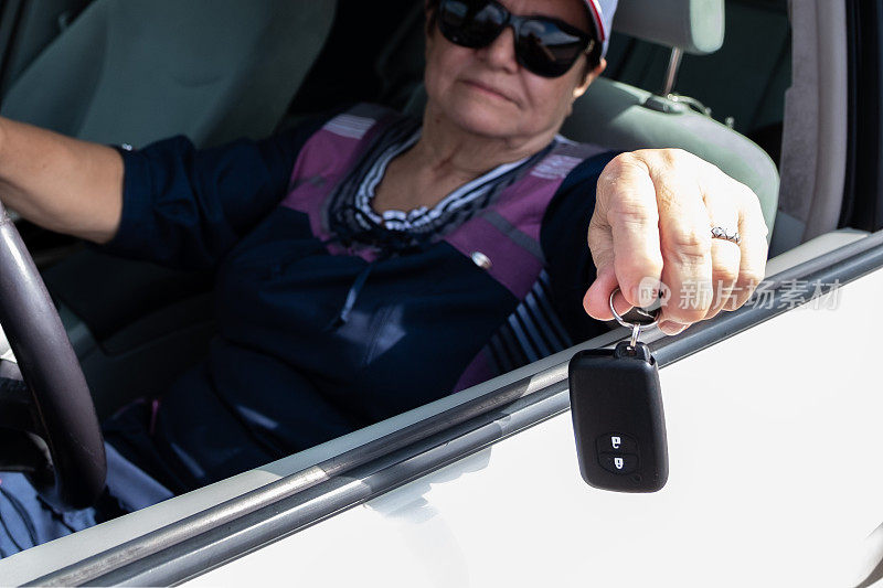 一位77岁的老妇人开着车，看着窗外，手里拿着车钥匙。