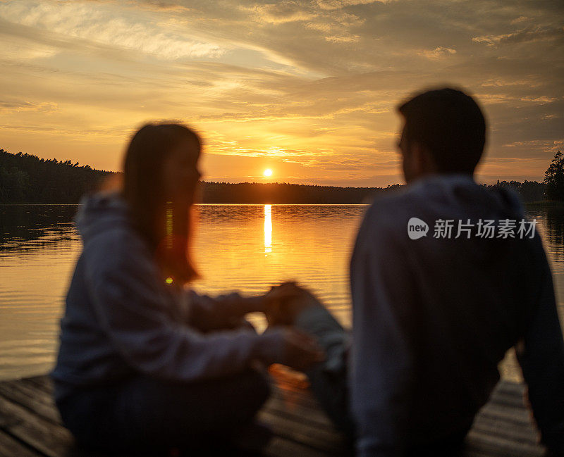 一对浪漫的情侣在码头上放松。在湖边欣赏日落的景色