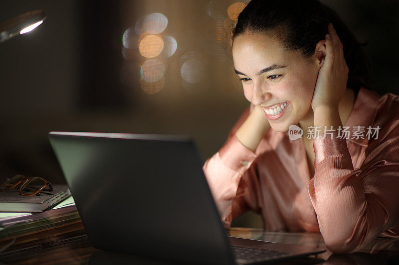 快乐的女商人在晚上用笔记本电脑