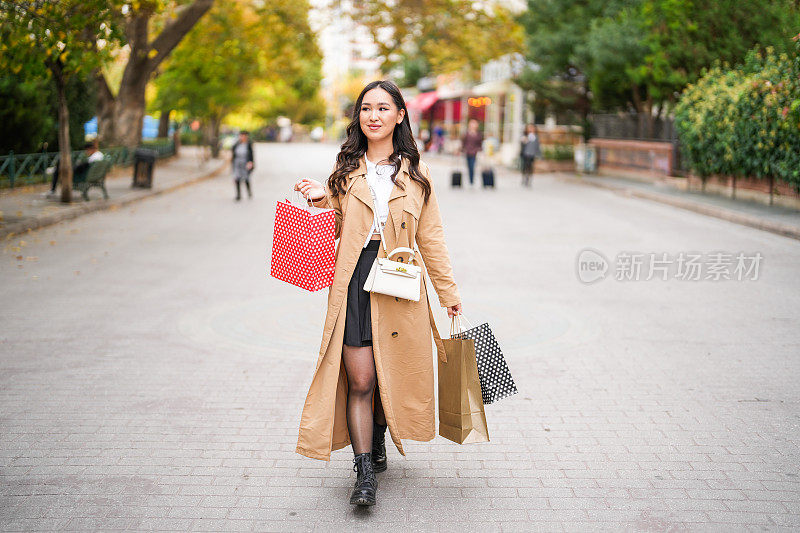 年轻的亚洲女人在街上拎着购物袋。购物的概念