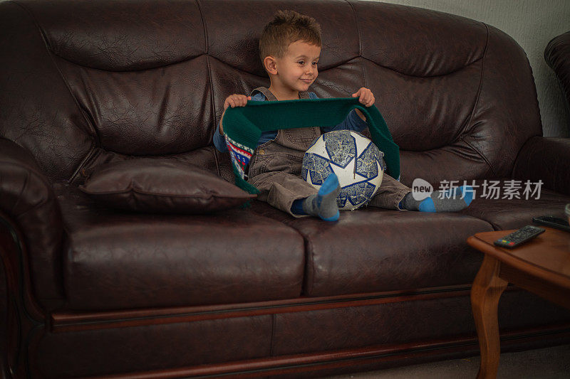 一个小男孩正在家里看电视上的足球比赛