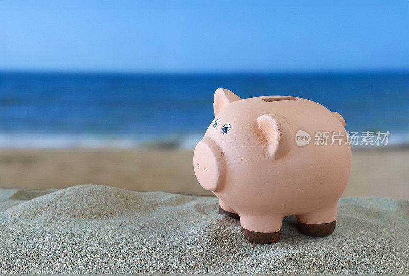 陶瓷猪硬币银行的特写图像堆沙，沙滩背景与海浪在低潮，大海和海岸线，重点放在前景，假期和度假储蓄的概念