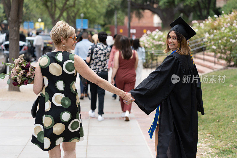 年轻微笑的大学生牵着妈妈的手走路