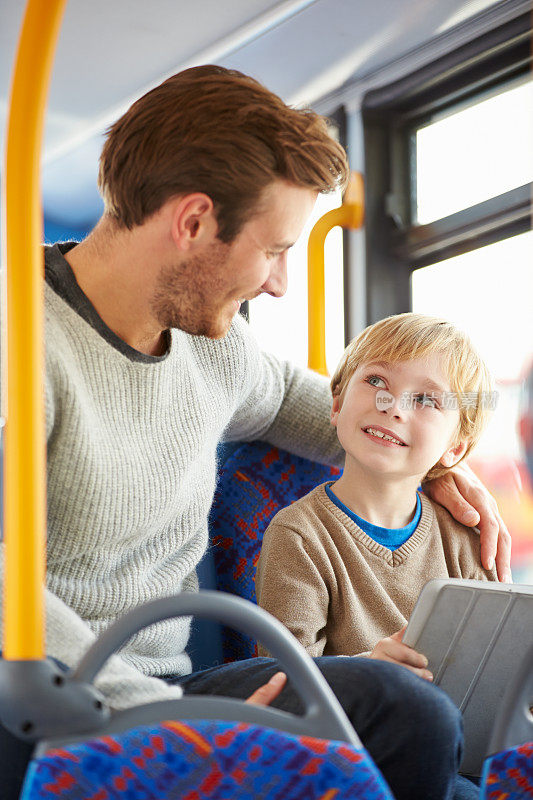 儿子在公车上和父亲一起使用平板电脑