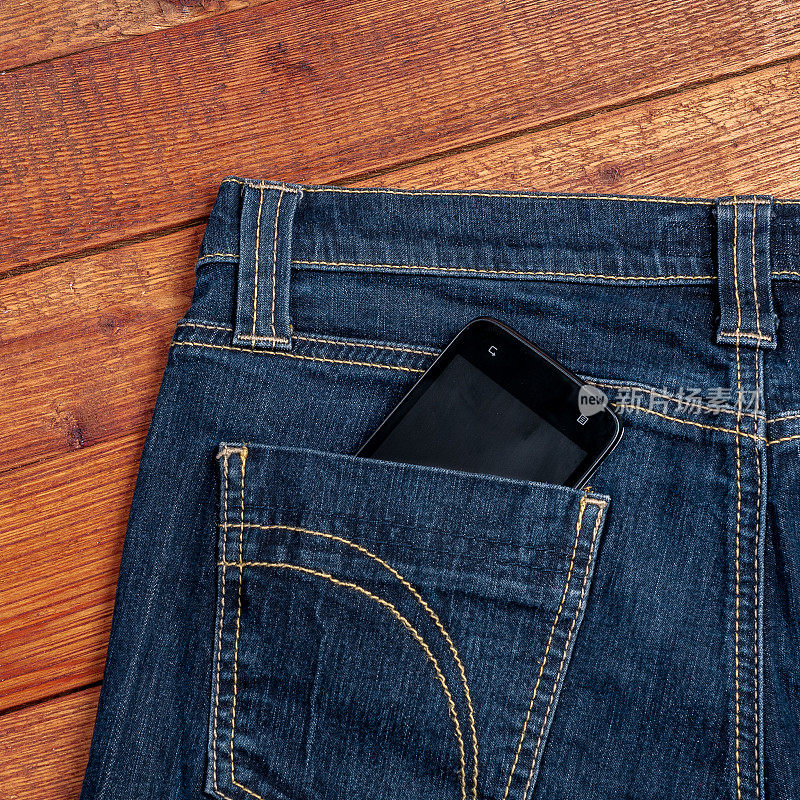 木头背景的旧牛仔裤口袋里的智能手机