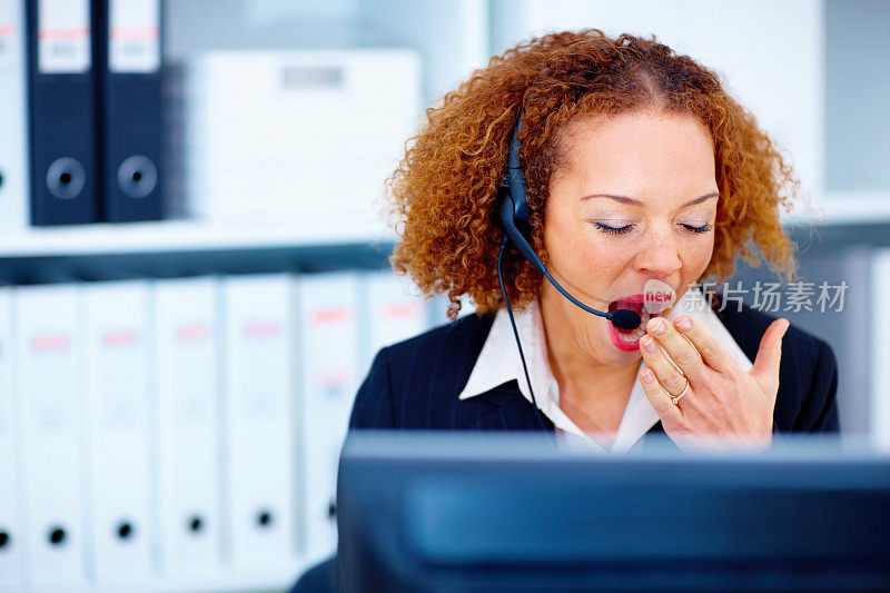 疲惫的商务女性在办公室使用耳机时打哈欠