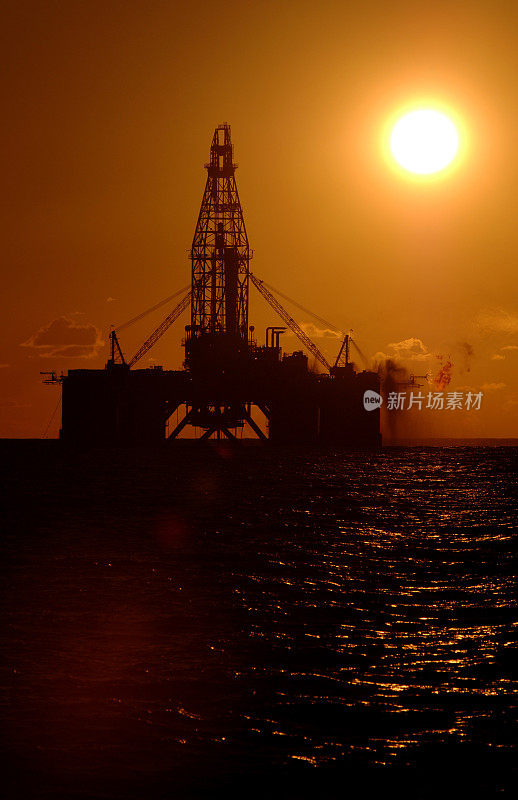 日落时海洋石油钻井平台的剪影。