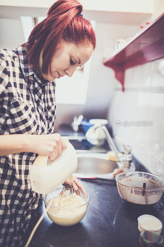 一个妇女用电动搅拌器搅拌液体面团来烘焙