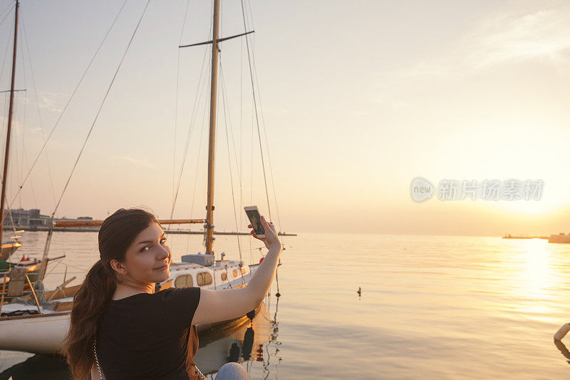 年轻女子在海上帆船上自拍日落