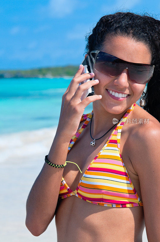 一个年轻女人在热带海滩上拿着手机