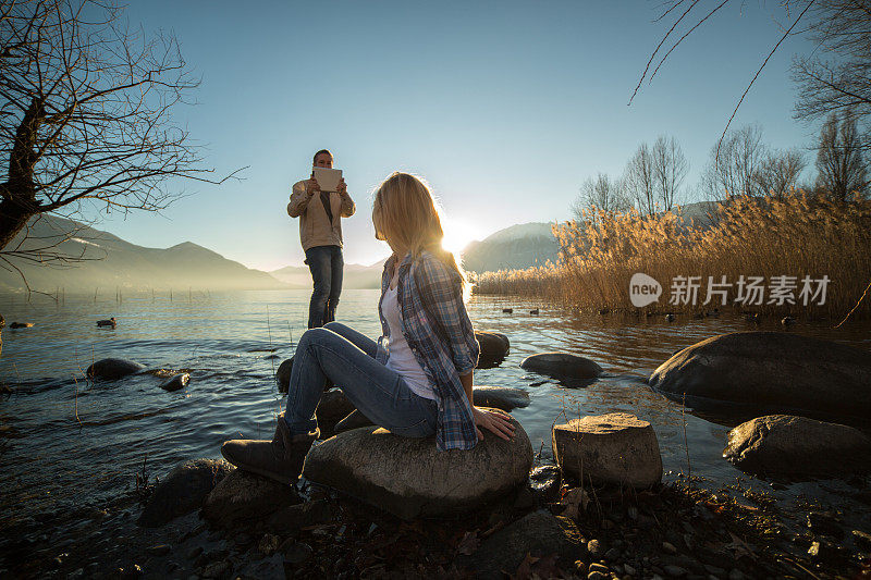 一对年轻夫妇在湖边用写字板拍照，欣赏大自然