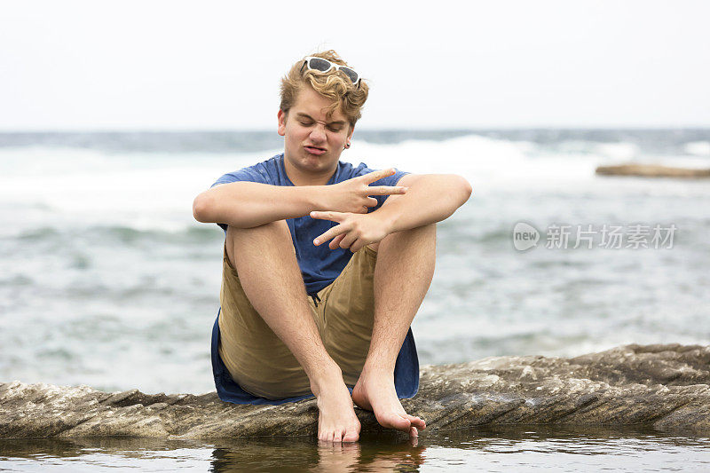 一个十几岁的男孩坐在石头上做笑脸和胜利的手势