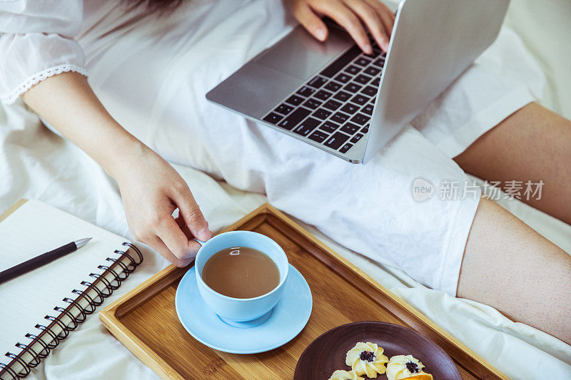 一个女人在床上用笔记本电脑喝咖啡
