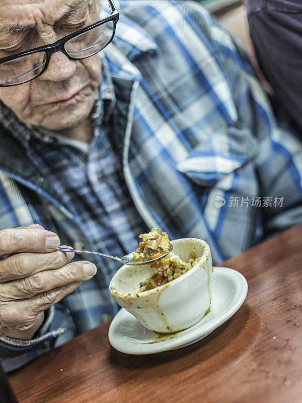 爷爷正在用勺子吃午饭汤和饼干